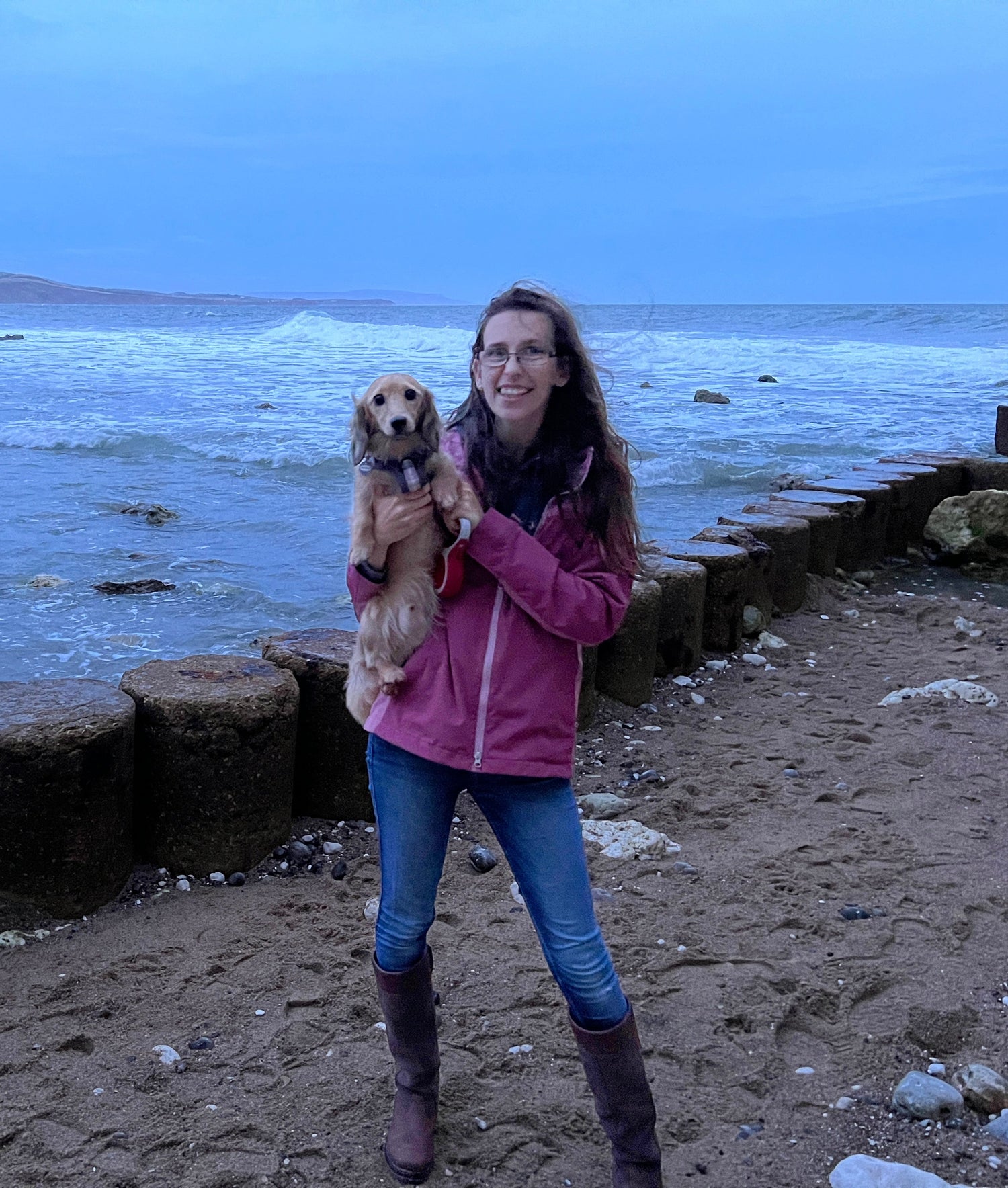 Woman holding a dog on a beach with ocean and cliffs in the background